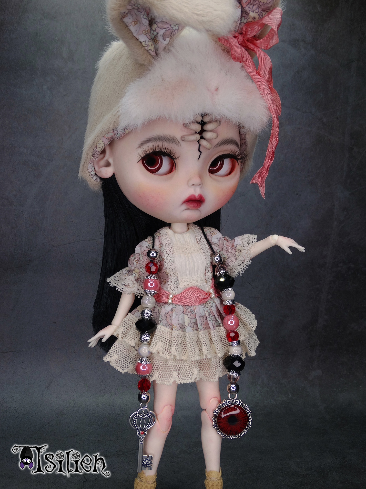 Amara, muñeca Blythe custom de aspecto siniestro y dulce, con pelo negro, vestido vintage y gorrito con orejas de conejo. Unos dedos abren una grieta en su frente, dejando ver un misterioso ojo.