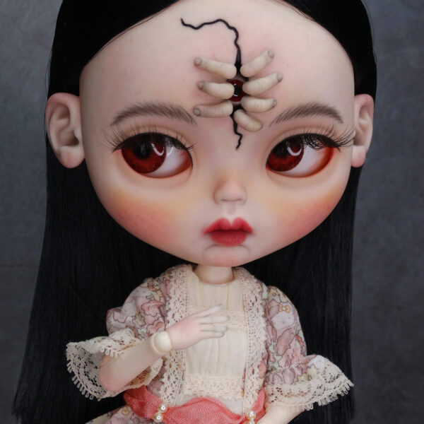 Amara, muñeca Blythe custom de aspecto siniestro y dulce, con pelo negro, vestido vintage y gorrito con orejas de conejo. Unos dedos abren una grieta en su frente, dejando ver un misterioso ojo.