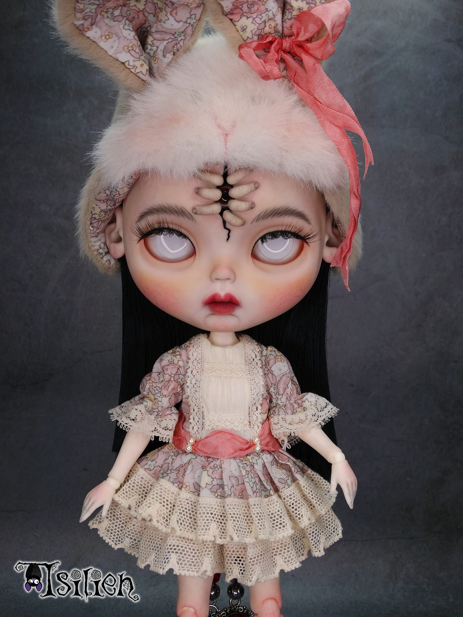 Amara, muñeca Blythe custom de aspecto siniestro y dulce, con pelo negro, vestido vintage y gorrito con orejas de conejo. Unos dedos abren una grieta en su frente, dejando ver un misterioso ojo.