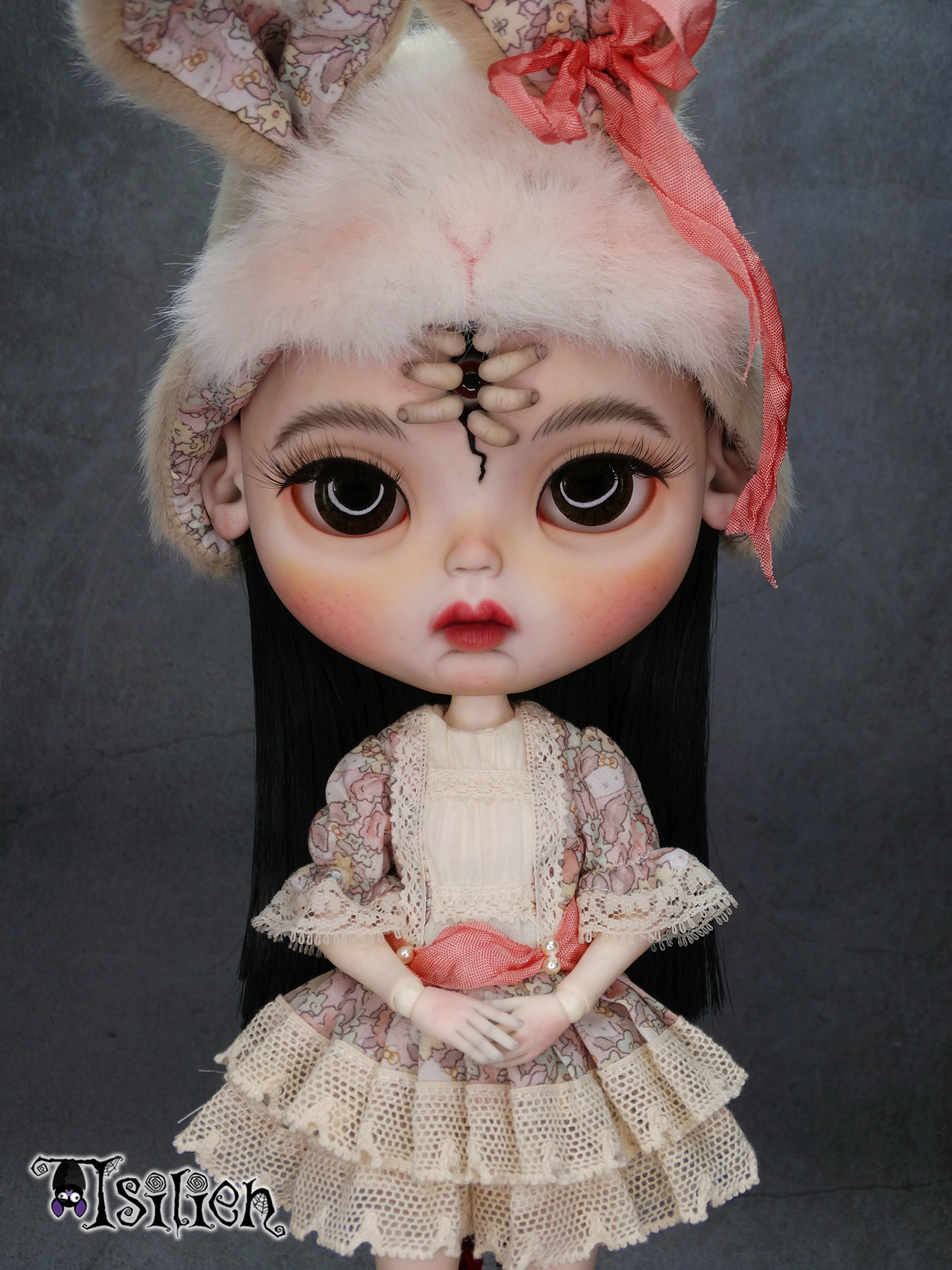 Amara, muñeca Blythe custom de aspecto siniestro y dulce, con pelo negro, vestido vintage y gorrito con orejas de conejo. Unos dedos abren una grieta en su frente, dejando ver un misterioso ojo.